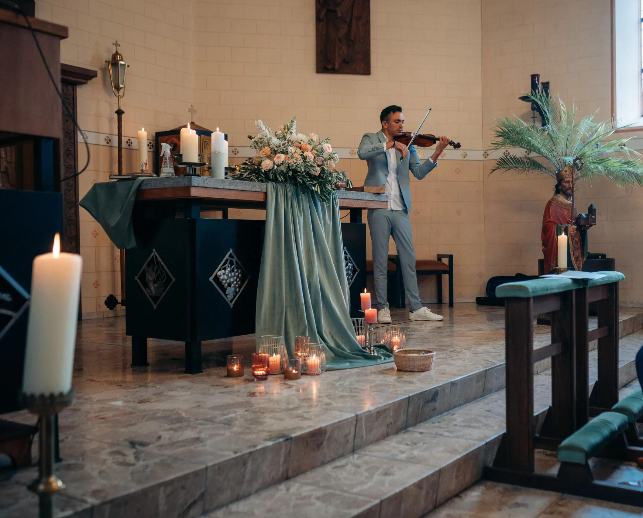 Martin Guha spielt Geigenmusik während einer kirchlichen Trauung zum Einzug der Braut, neben dem romantisch geschmückten Altar.